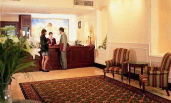 a hotel lobby with a reception desk , a couch , and two people standing near the counter at Midland Hotel, Bradford