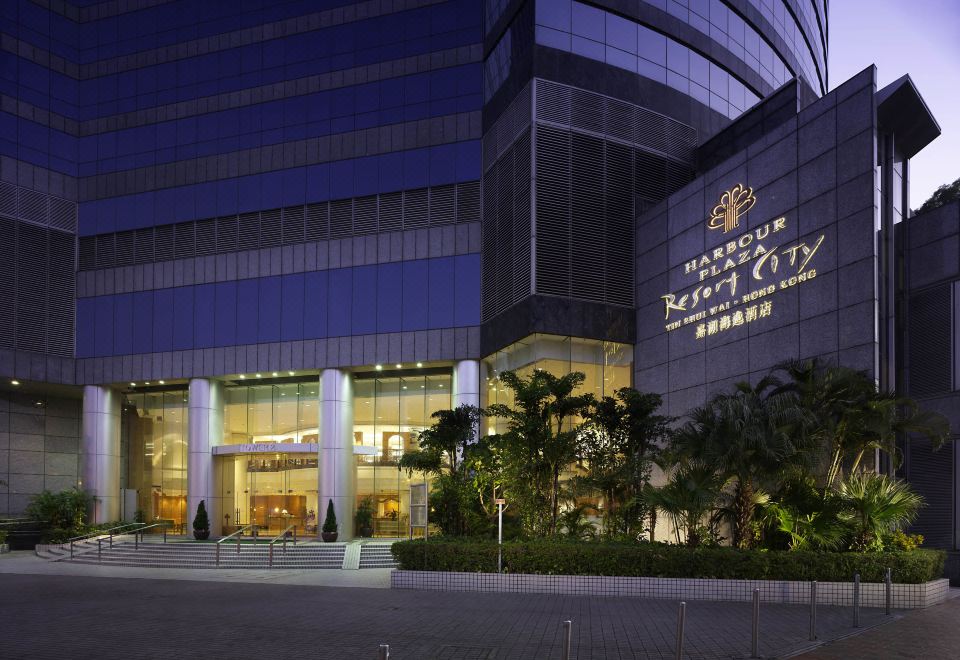 At night, the front entrance of a hotel is illuminated by its glass facade and stone cladding at Harbour Plaza Resort City
