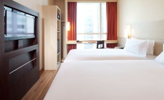 The bedroom features a double bed, a desk, and a chair positioned in front of a large window with a view of the surroundings at ibis Hong Kong Central and Sheung Wan Hotel