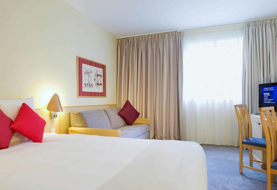 a hotel room with a large bed , yellow and red pillows , a couch , and a dining table at Novotel Manchester West