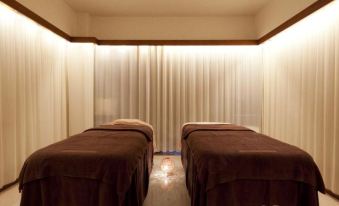 a room with two massage tables covered in brown blankets , surrounded by white curtains and lit by recessed lighting at Hotel Resol Gifu