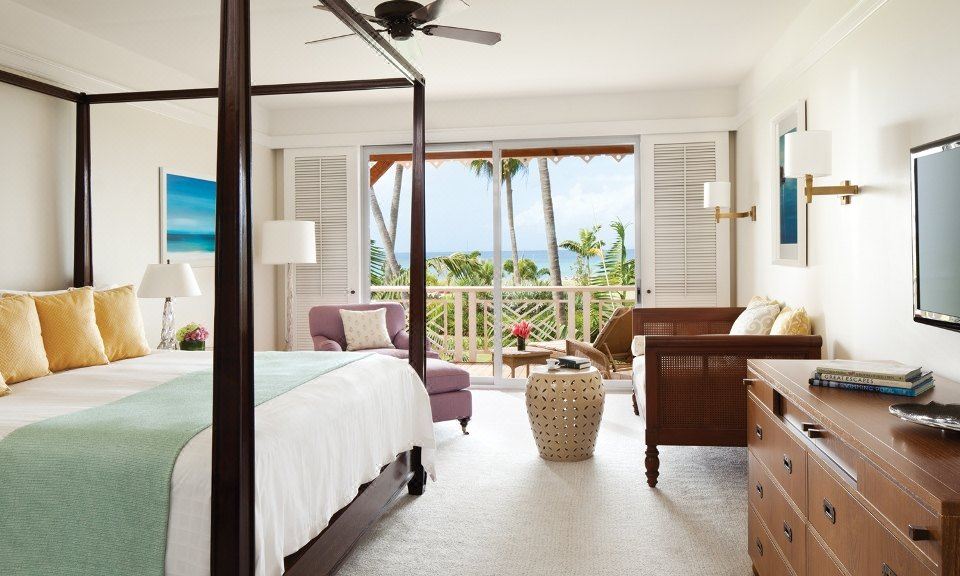 a spacious bedroom with a king - sized bed , a large window , and a view of the ocean at Four Seasons Resort Nevis