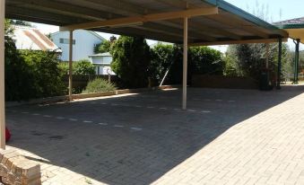 a large , empty parking lot under a covered area with trees and buildings in the background at Adelong Motel