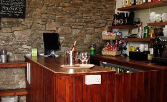 a wooden bar with a wine glass , bottle , and glasses on it , as well as a shelf filled with wine bottles at YHA Brecon Beacons Danywenallt