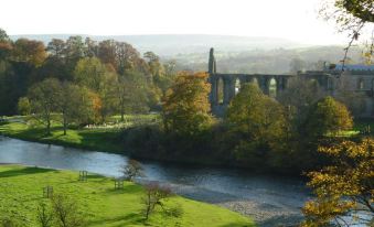 a serene landscape of a river flowing through a lush green field , with a stone bridge spanning across the river at Ashfield House