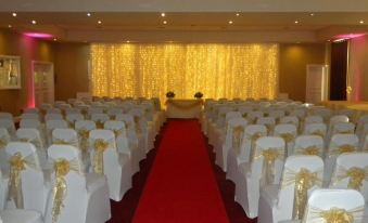 a large room with rows of white chairs arranged in a symmetrical pattern , illuminated by yellow lights at Cairn Hotel