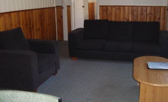 a living room with a couch and chair , wooden walls , and a carpet on the floor at Nrma Halls Gap Holiday Park