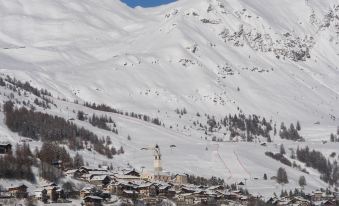 a snowy mountain village with a church in the foreground and skis and snowboards on the slopes at Santa San