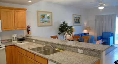 a kitchen with a granite countertop , sink , and dining table in the background , along with pictures hanging on the wall at Wyndham Reef Resort Grand Cayman