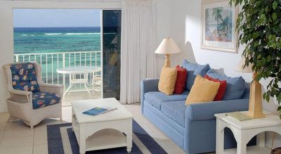 a living room with a blue couch , white coffee table , and a view of the ocean through a sliding glass door at Wyndham Reef Resort Grand Cayman