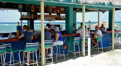 a group of people sitting at a bar with blue and green chairs around it at Wyndham Reef Resort Grand Cayman