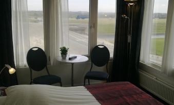 a hotel room with a bed , two chairs , and a table near the window overlooking a grassy field at Hotel Savoy