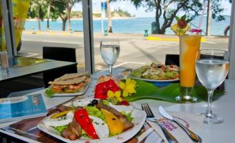 a table with plates of food , a glass of wine , and a glass of juice is set up outside near the water at Hotel Beaurivage