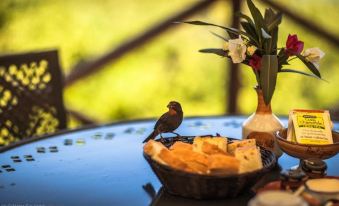 a bird is perched on a table with a basket of bread and a vase of flowers at Harmony Hall