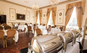 a large dining room with multiple tables covered in white tablecloths , surrounded by gold chandeliers and elegant decorations at Melville Castle Hotel