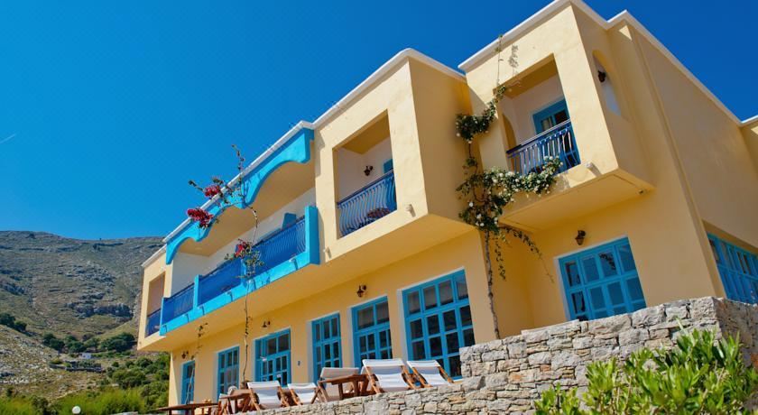 a yellow and blue building with a swimming pool in front of it , surrounded by trees at Pedi Beach Hotel