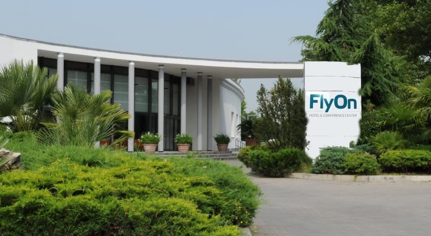 the entrance of a modern building with a curved roof and green plants , under a clear blue sky at FlyOn Hotel & Conference Center