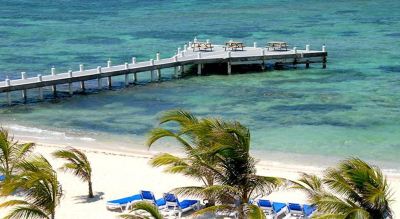 a tropical beach with clear blue water , white sand , and palm trees , as well as several lounge chairs and umbrellas set up for relaxation at Wyndham Reef Resort Grand Cayman