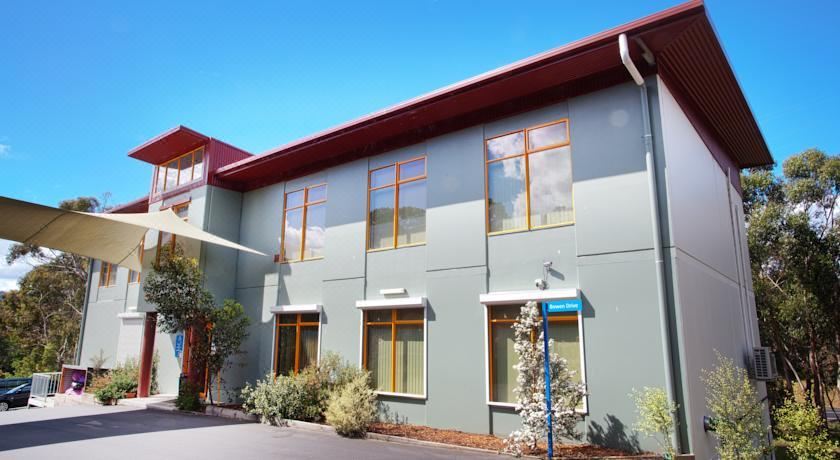 a gray building with multiple windows and a red roof , situated in front of trees and bushes at Discovery Parks - Hobart