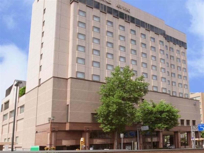 a tall hotel building surrounded by trees on a city street , with the sun setting in the background at Hotel Metropolitan Morioka New Wing