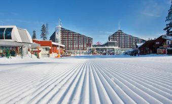 a snow - covered ski slope with a hotel in the background , surrounded by trees and other buildings at Rila Hotel Borovets