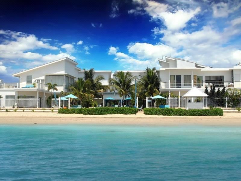 a large white house situated on the beach , surrounded by palm trees and clear blue water at Ocean View Residence