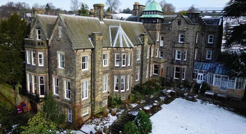 an old stone building with a green dome , surrounded by snow - covered trees and a garden at Makeney Hall Hotel