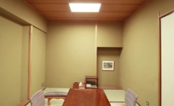 a room with a wooden table and chairs , white walls , and a wooden ceiling with light at Kawana Hotel