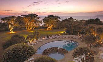 a luxurious hotel with a large pool surrounded by lounge chairs and trees , during sunset at The Atlantic Hotel