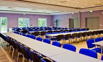 a large conference room with rows of blue chairs and white tables , set up for an event at Best Western Hotel Jurata