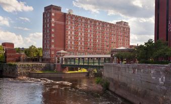 a large brick building with a river in front of it and a yellow boat nearby at UMass Lowell Inn and Conference Center