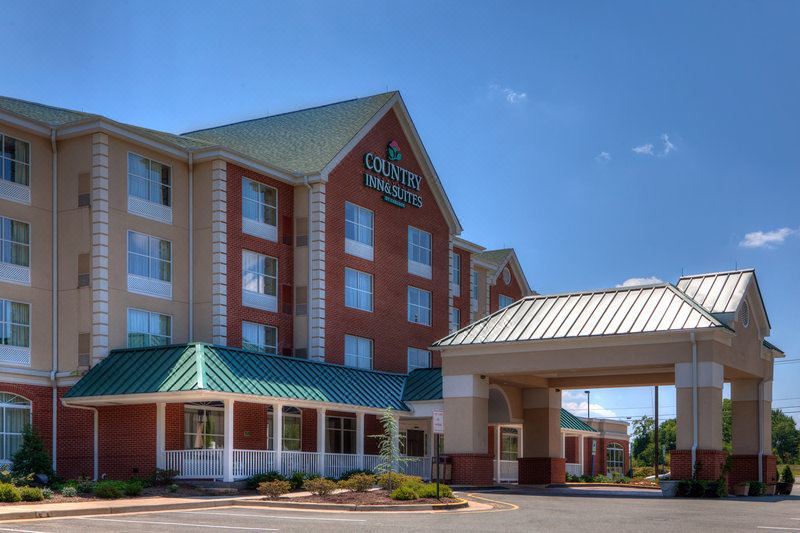 a holiday inn express hotel with its distinctive red - brick exterior , standing under a clear blue sky at Country Inn & Suites by Radisson, Fredericksburg, VA