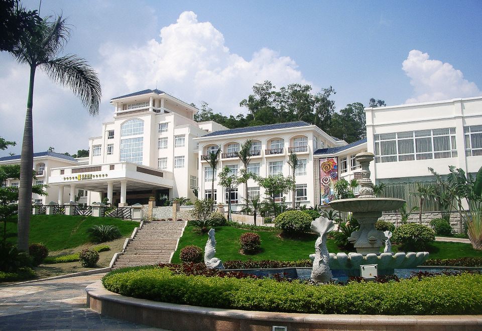 a large white building surrounded by greenery and a fountain in front of it , with a fountain in the background at Royal Hotel