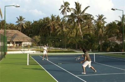 a man and a woman are playing tennis on an outdoor court , surrounded by palm trees at Vilamendhoo Island Resort & Spa