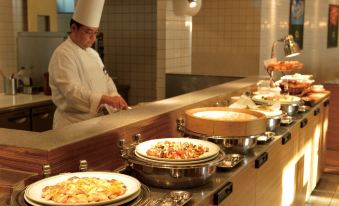 a chef in a restaurant kitchen preparing food on a dining table , surrounded by various dishes and utensils at Loisir Hotel Naha