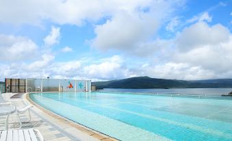 a large outdoor swimming pool surrounded by grass and trees , with mountains in the background at New Akan Hotel